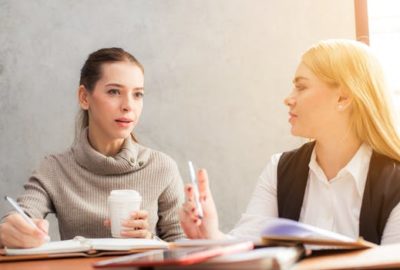 Two female students sit at desk discussing jobs in betting industry.